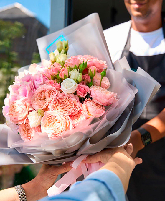 Florista entregando a un cliente bouquet de flores rosadas
