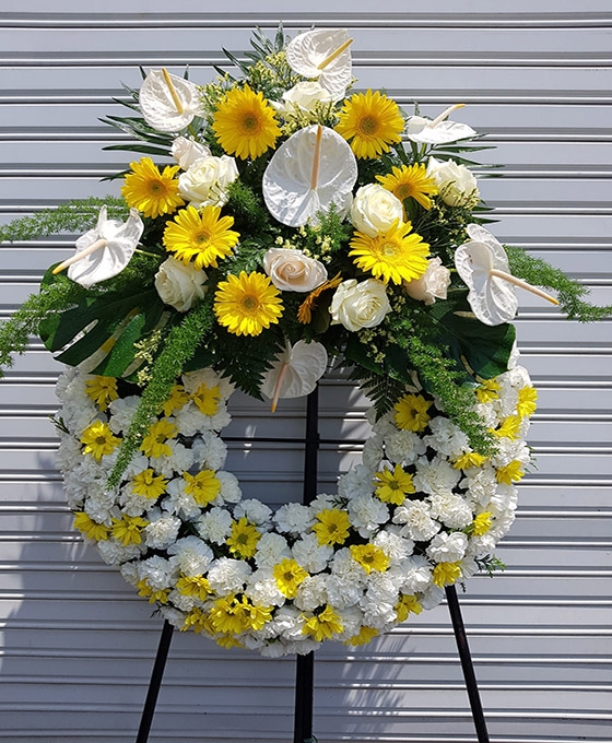 Corona de flores funerarias en tonos amarillos y blanco, con verdes